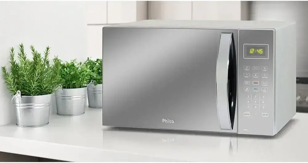 Micro-ondas em uma cozinha moderna com elementos claros e plantas decorativas.
